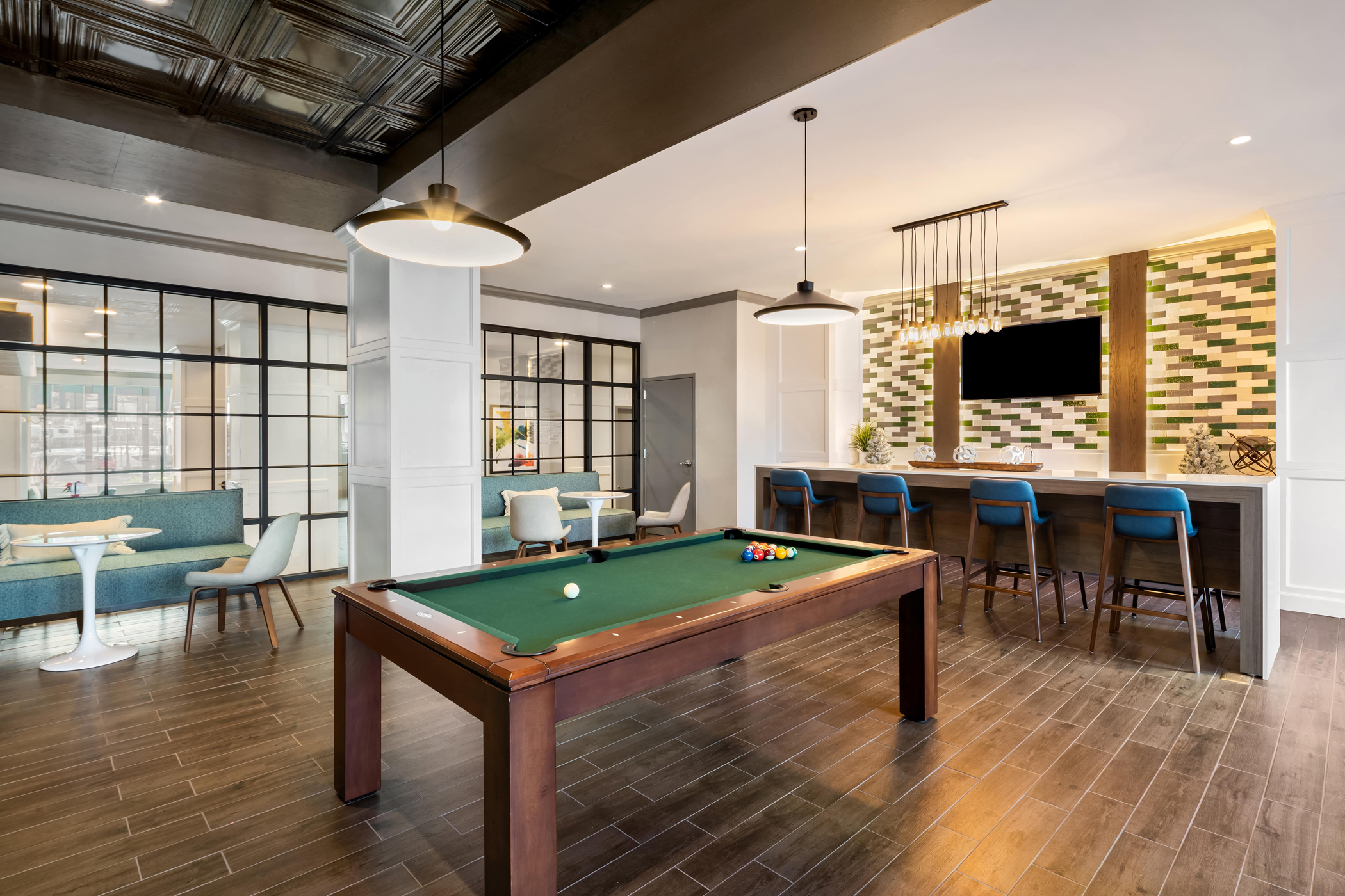 A game room featuring a pool table, seating spaces and tables and a dining and kitchen area.