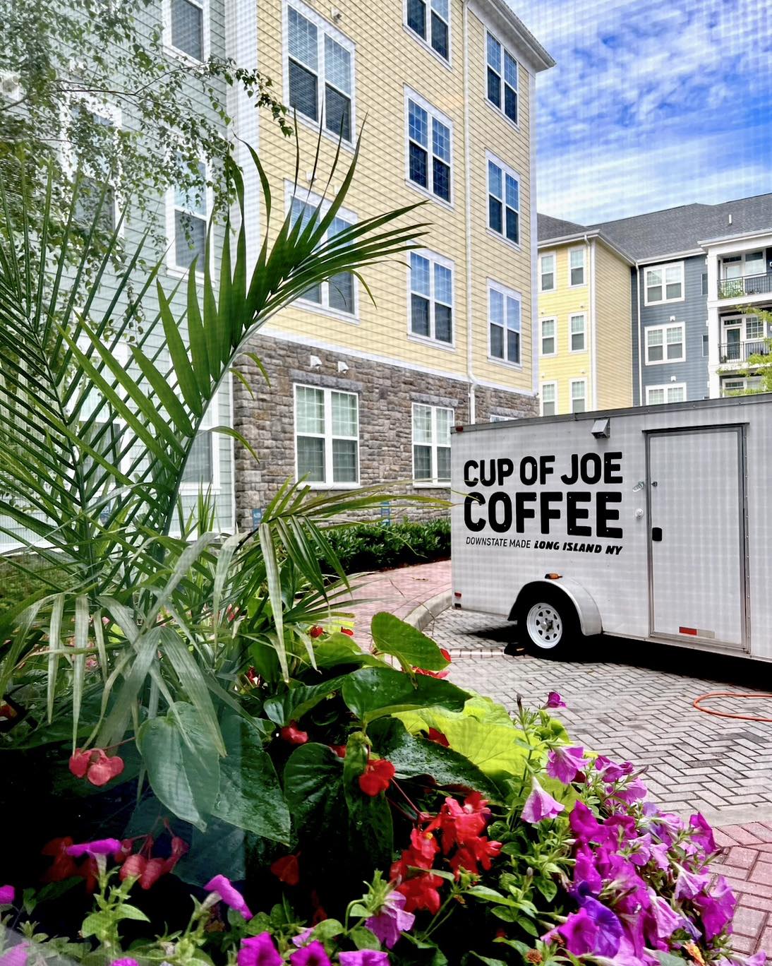 A picture of the Cup of Joe Coffee food truck taken from behind a glass and floral garden.