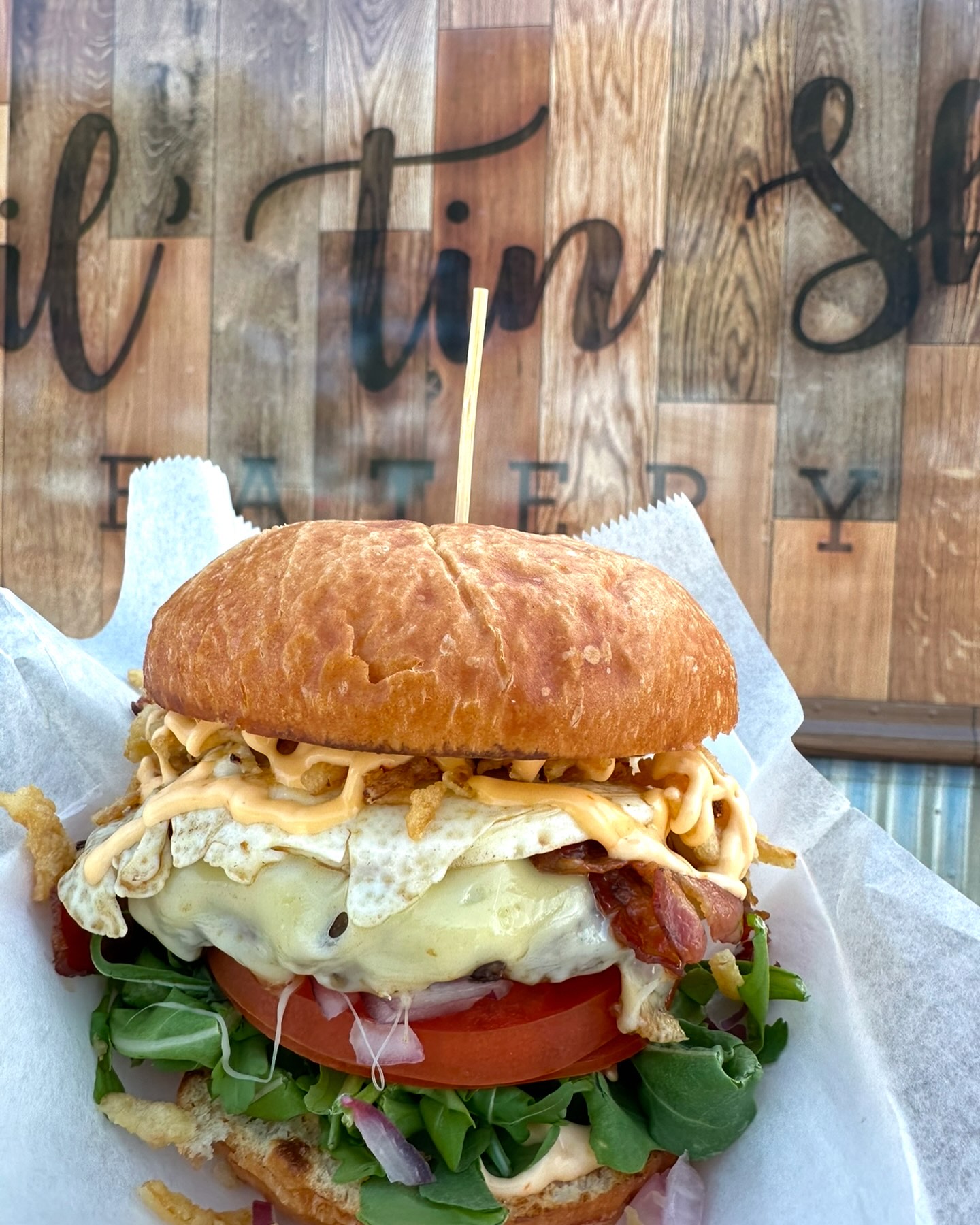 Burger with egg, patty, cheese, tomato, lettuce, and two buns with a toothpick in between