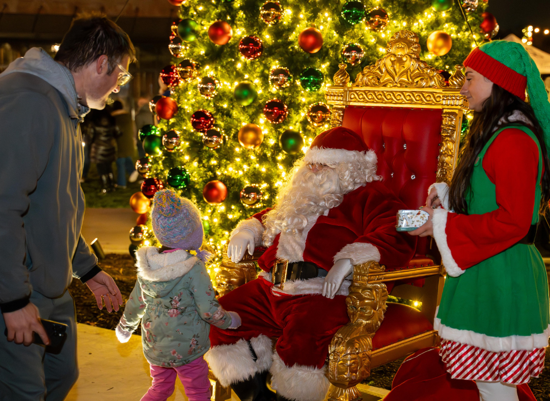 Santa greeting a child in front of a Christmas tree