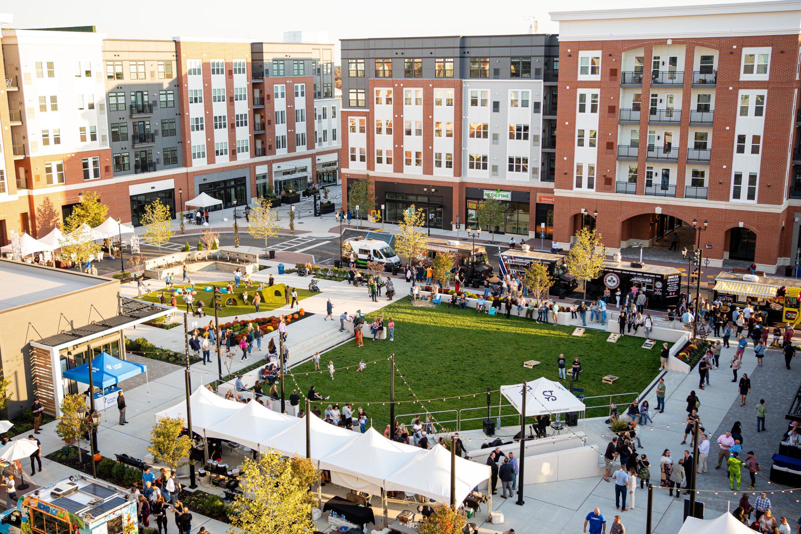 Aerial shot of the Village Green at Station Yards during the summer concert series with a band playing on stage and visitors hanging out on the grass