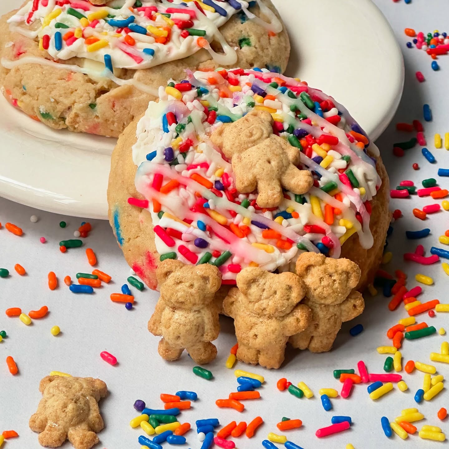 Two confetti cookies with vanilla icing and multicolored sprinkles with teddy grahams